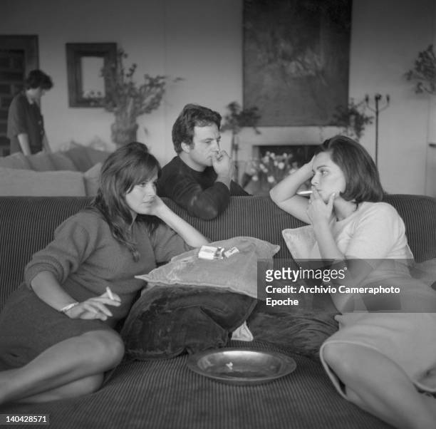 Italian actress Lucia Bose with Franco Interlenghi and Antonella Lualdi sitting on a sofa and smoking a cigarette, Madrid, 1961.