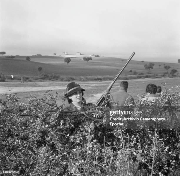 Italian actress Lucia Bose hiding behind a bush during a hunting trip, Madrid, 1961.