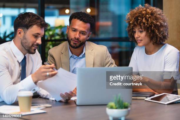 three business people meeting and looking at a laptop and a document. - signing mortgage stock pictures, royalty-free photos & images