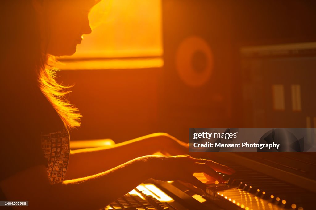 Woman music producer playing piano in evening in recording music studio