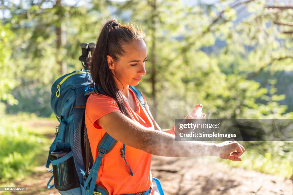 A woman applies mosquito spray to her hands during hiking.