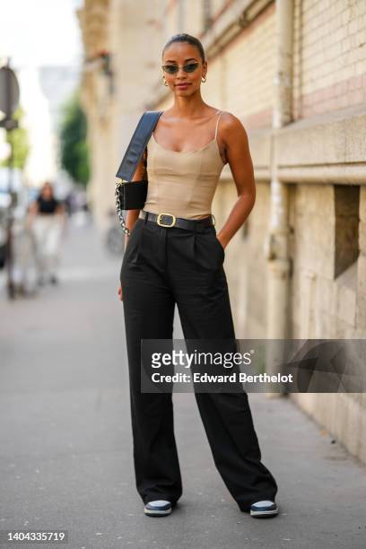 Flora Coquerel wears black cat eyes sunglasses, a beige corset square-neck tank-top, a black shiny leather shoulder bag, a black shiny leather belt,...