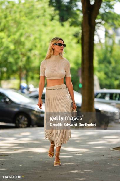 Natalia Verza wears black sunglasses from Valentino, gold large logo pendant earrings from Fendi, a beige ribbed short sleeves / turtleneck cropped...