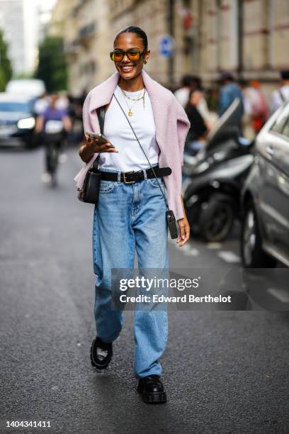 Guest wears orange sunglasses, gold earrings, a white halter-neck tank-top, gold chain pendant necklaces, a pale pink wool pullover, a black shiny...