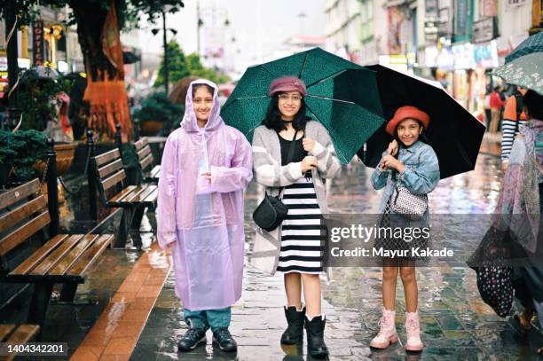 three girls standing with their umbrellas on the city street - monzón fotografías e imágenes de stock