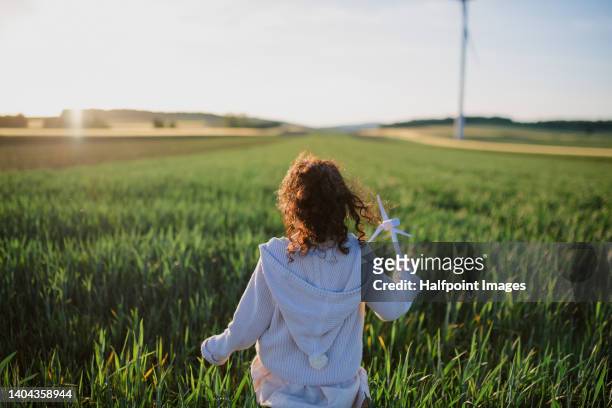 rear view of little girl standing in field with model of wind turbine. concept of ecology future and renewable resources. - international day one stock pictures, royalty-free photos & images
