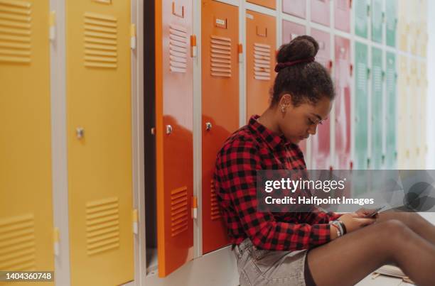 sad multiracial student girl sitting in school locker room, using smartphone. - inside locker stock pictures, royalty-free photos & images