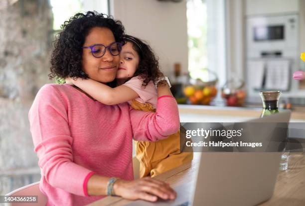 multiracial girl with her mother hugging, having fun in kitchen during home-office and homeschooling time. - mother and child fotografías e imágenes de stock