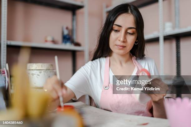 beautiful young woman is painting a ceramic mug in workshop - art and craft stock pictures, royalty-free photos & images