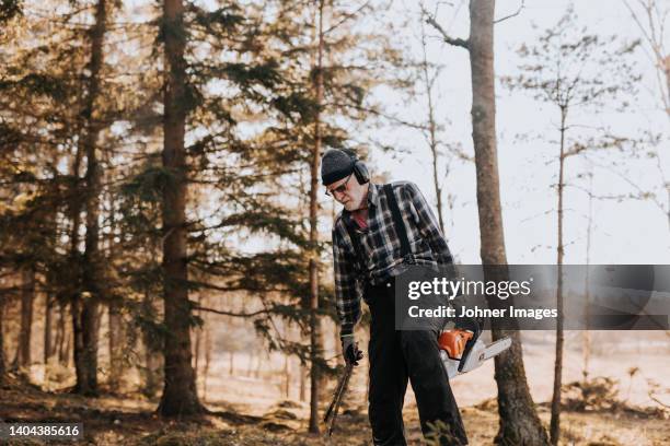 senior man in forest holding chainsaw - forestry worker stock-fotos und bilder