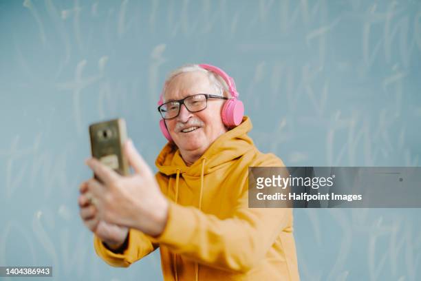 senior man taking selfie with smartphone, posing in photo studio. - cooler opa stock-fotos und bilder