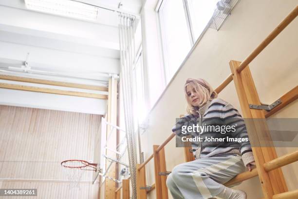 girl sitting on climbing frame in school gym - climbing frame stockfoto's en -beelden