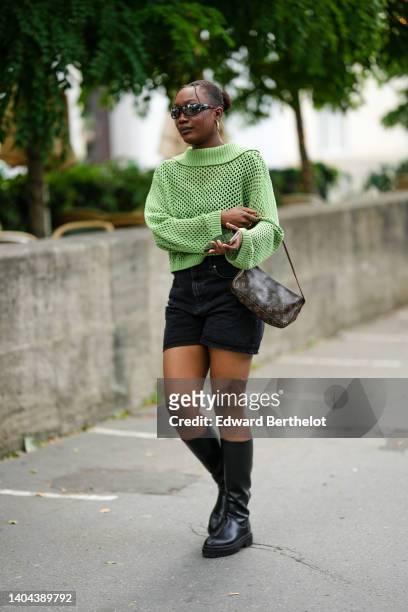 Guest wears black sunglasses, gold earrings, a pale green mesh pullover, black denim shorts, a brown LV monogram print pattern in coated canvas...