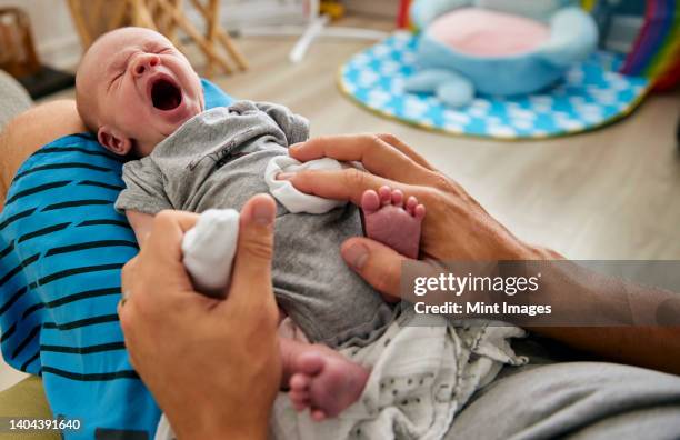 father's hands holding three month old baby boy yawning on lap, indoors - lying on back ストックフォトと画像