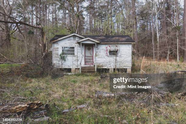 a rural homestead or small house abandoned and crumbling, overgrown with plants and shrubs - run down stock pictures, royalty-free photos & images