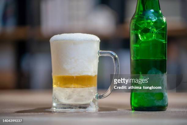 ice cold glass of beer with overflowing foam and  green bottle. - pilsner - fotografias e filmes do acervo