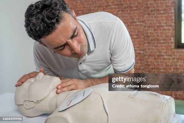 first-aider practising chest compressions on a cpr training dummy. - aider stock pictures, royalty-free photos & images