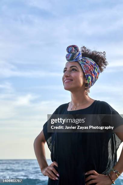 portrait of carefree moroccan woman wearing cuban scarf at sunset on beach - moroccan woman stock pictures, royalty-free photos & images