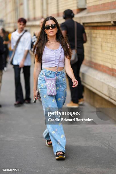 Guest wears black sunglasses, silver earrings, white and gold pearls necklace, a gold chain necklace, a pale purple striped print pattern short...