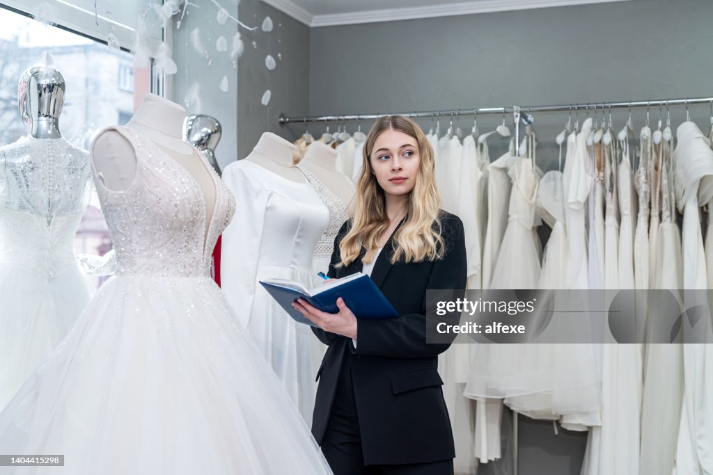 Pretty young saleswoman hold notes diary in modern wedding store