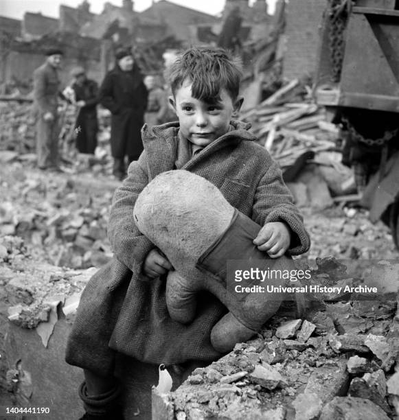 Abandoned boy holding a stuffed toy animal amid ruins following German aerial bombing of London, 1941.