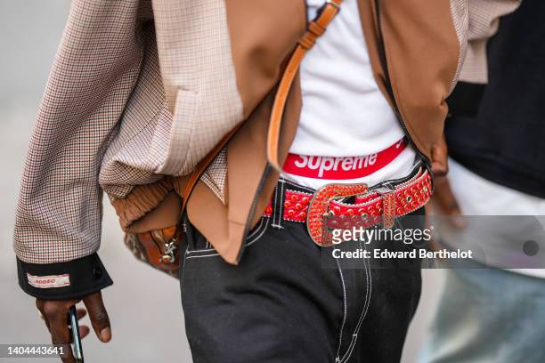 Guest wears a white tank-top, a brown and checkered print pattern oversized bomber coat, a white Supreme boxer, a red shiny embroidered rhinestones...