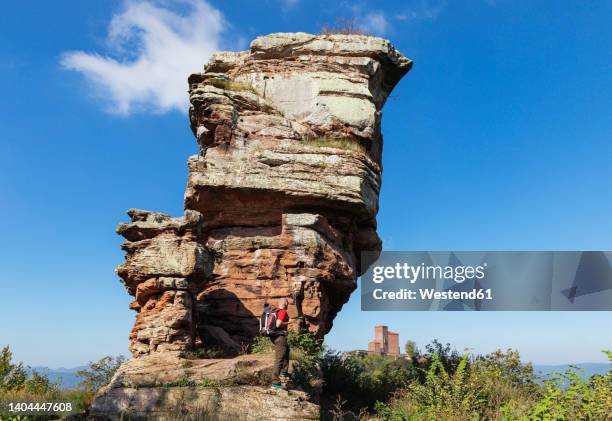 germany, rhineland-palatinate, senior hiker standing in front of sandstone rock formation in palatinate forest with trifels castle in distant background - rhineland palatinate stock pictures, royalty-free photos & images