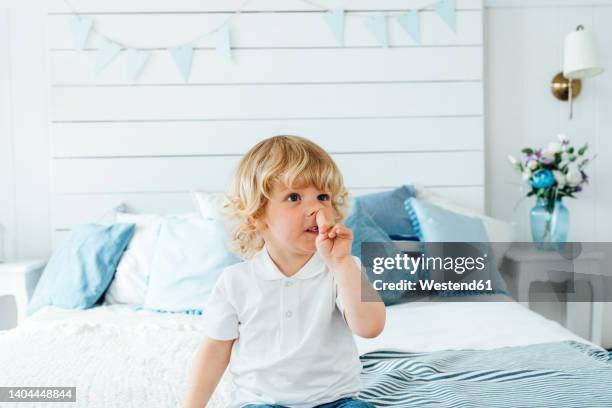 boy picking nose sitting on bed at home - mettersi le dita nel naso foto e immagini stock
