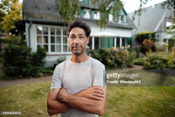 mature man with arms crossed standing in front of house - voor of achtertuin stockfoto's en -beelden