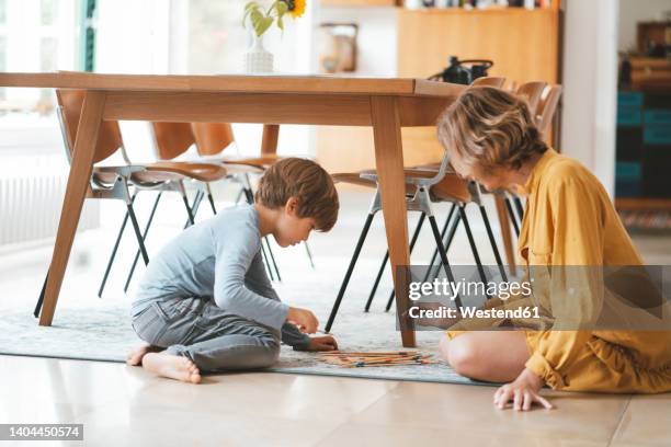 mother with son playing mikado sitting by dining table at home - mikado stock pictures, royalty-free photos & images