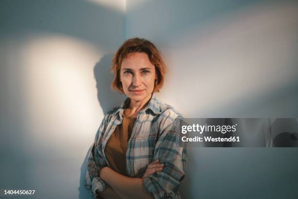 smiling woman with arms crossed standing in front of wall - einzelne frau über 40 stock-fotos und bilder