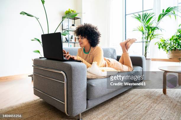 young woman using laptop lying on sofa at home - enkels over elkaar stockfoto's en -beelden