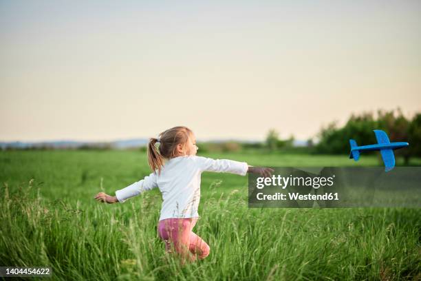 playful girl throwing airplane in agricultural field - toy airplane stock-fotos und bilder