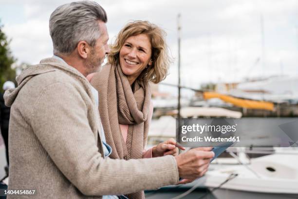 smiling woman talking with man holding tablet pc at harbor - mann vor pc stock-fotos und bilder