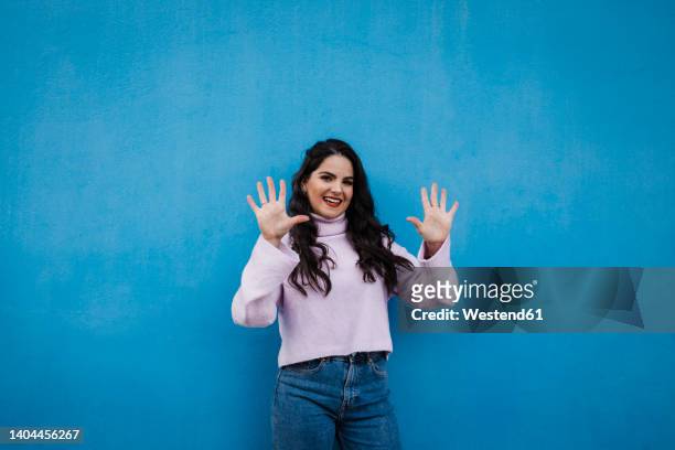 smiling young beautiful woman showing number 10 in front of blue wall - counting imagens e fotografias de stock