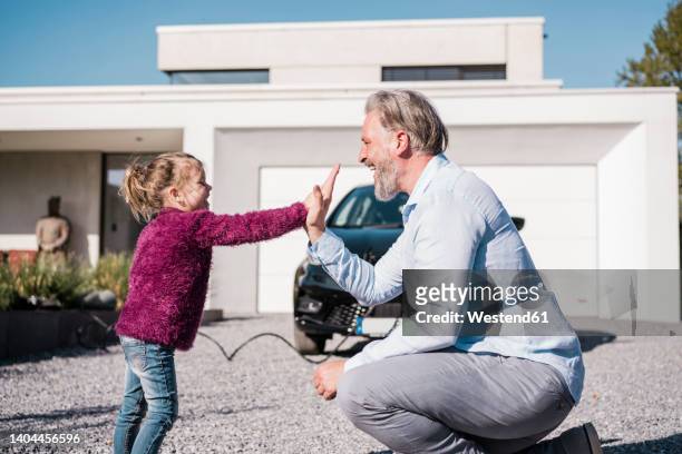 happy girl giving high five to father in front of car on sunny day - umweltfahrzeug stock-fotos und bilder