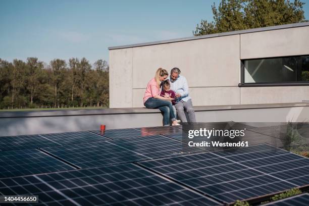 man and woman with daughter sitting on wall by solar panel - family in front of house stock-fotos und bilder
