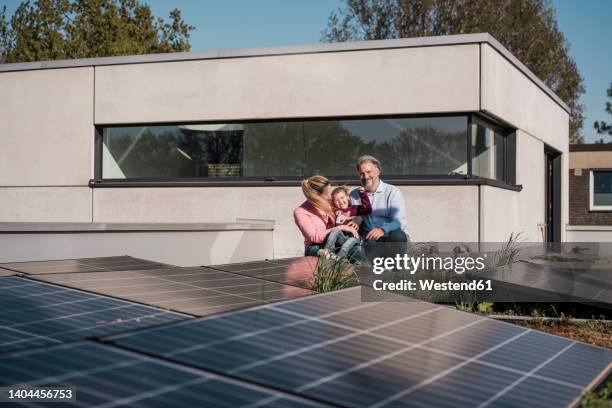 happy girl with parents sitting by solar panel on rooftop - pannello solare foto e immagini stock