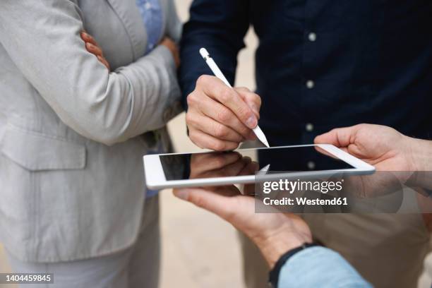hand of businessman signing on tablet pc standing by colleagues - digitized pen stock pictures, royalty-free photos & images