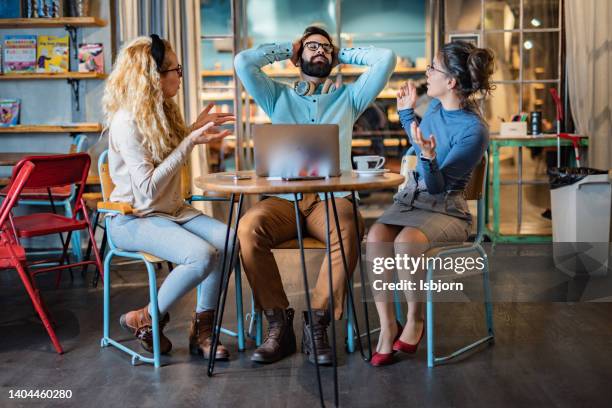 zwei kolleginnen streiten sich mit männlichem kollegen im café - male student wearing glasses with friends stock-fotos und bilder