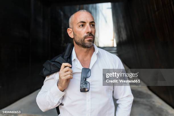 man carrying jacket standing in alley - one mid adult man only stock pictures, royalty-free photos & images