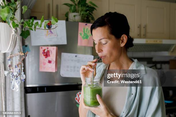 woman drinking healthy smoothie from straw at home - drinking juice stock-fotos und bilder