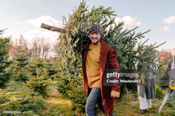 man carrying christmas tree on shoulder at farm - christmas decorations in store stock pictures, royalty-free photos & images