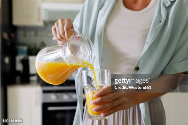 hands of woman pouring fresh orange juice in glass from jug - vruchtensap stockfoto's en -beelden