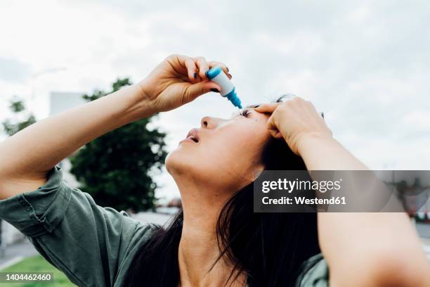 young woman putting drop in eye - colírio imagens e fotografias de stock