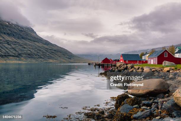 eskifjordur is a charming seaside village in the mid of the eastern fjords and the red-colored and well-preserved houses and fishing sheds lined up and down the shore provide an amazing view. - iceland foto e immagini stock