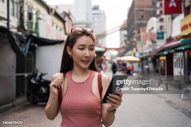 young asian woman using a smartphone while traveling in petaling street - kuala lumpur road stock pictures, royalty-free photos & images