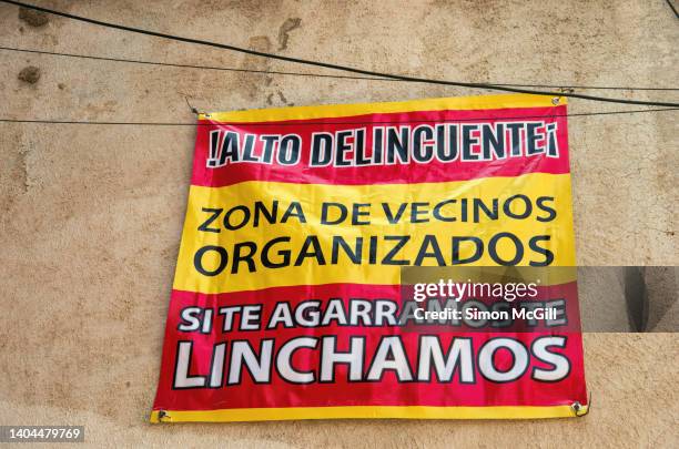 spanish-language banner sign stating '¡alto delincuente! zona de vecinos organizados. si te agarramos te linchamos.' [stop delinquent! organized neighborhood zone. if we catch you, we'll lynch you.] hanging on the exterior wall of a building - albert lynch stock-fotos und bilder