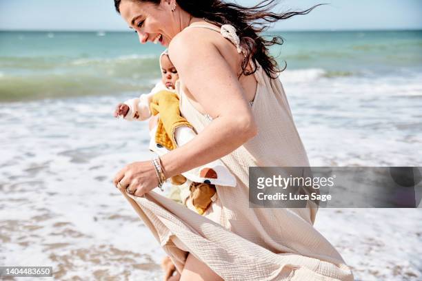 A mother with her baby in arms excitedly runs amid the incoming wave on a family trip to the beach