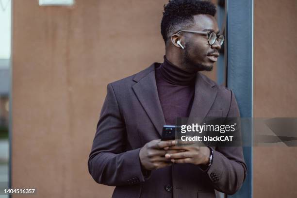 beaux hommes d’affaires afro-américains utilisant un téléphone portable dans la rue - in ear headphones photos et images de collection